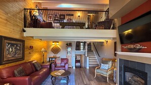 A spacious living room with a red leather sofa, a coffee table, and a fireplace. A staircase leads to an upper level with a balcony. - Make Memories - Just Steps to the Shuttle, Close to Base, and Locker at the Base (Steamboat Springs)