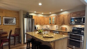 A modern kitchen with wooden cabinets, stainless steel appliances, and a granite island with bar stools. - Make Memories - Just Steps to the Shuttle, Close to Base, and Locker at the Base (Steamboat Springs)