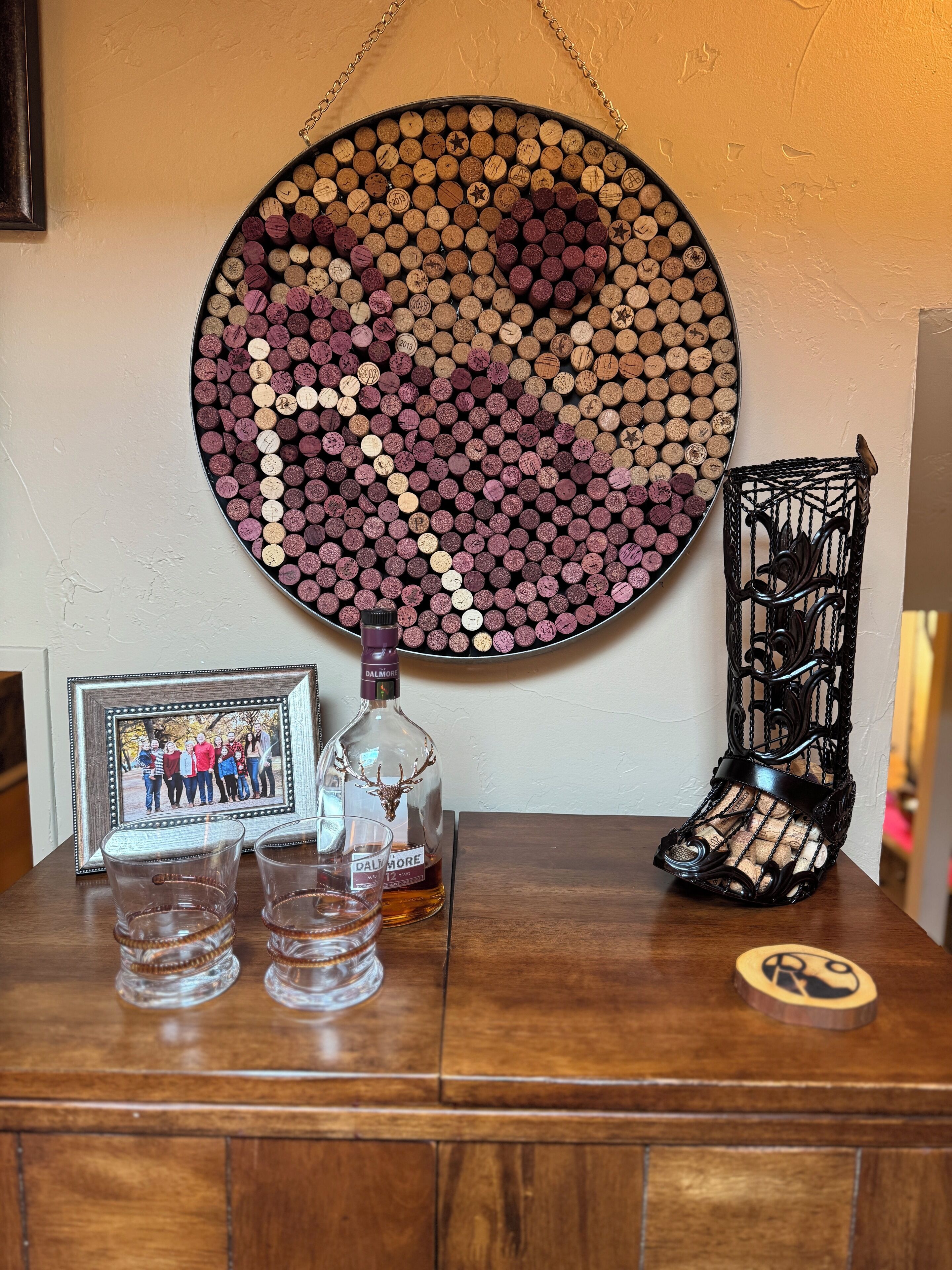 Et bord med en dekorativ korktavle, en flaske spiritus, glas, et indrammet foto og en dekorativ metalholder.