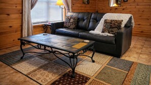 Interior acolhedor de uma cabana com um sofá de couro, uma mesa de centro estampada e diversos tapetes no chão.