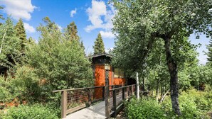 Un pont de fusta que condueix a un edifici amb façana de maó, envoltat de vegetació abundant i arbres.