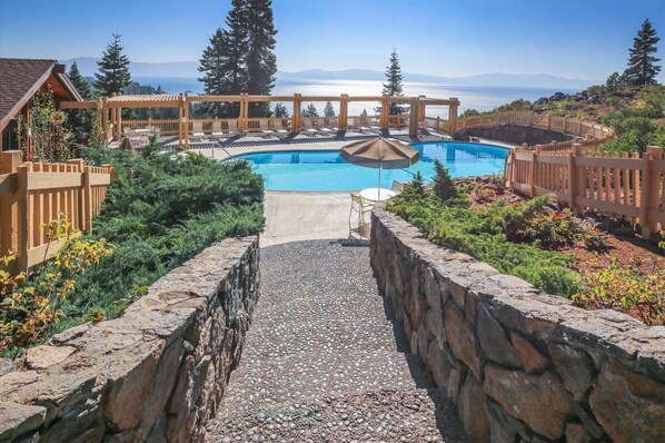 A pool area with a wooden pergola, stone walls, and a view of the ocean.