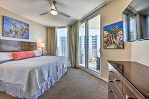 Ein Hotelzimmer mit einem großen Bett, einem Deckenventilator, einem Balkon mit Blick auf Gebäude und Kunstwerken an den Wänden.