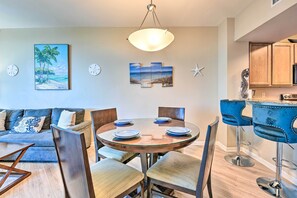 Ein modernes Wohnzimmer mit einem runden Glastisch, blauen Polsterstühlen, einem blauen Sofa und einem Gemälde mit Strandmotiv.