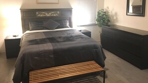 Une chambre à coucher comprenant un lit, des tables de chevet, une commode, un banc, une plante et un miroir accroché au mur.