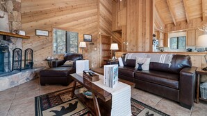 A cozy log cabin interior with a fireplace, leather sofa, and wooden walls. - Wolf View Lodge - Air Conditioning, Close to Slopes, Views, Fireplace, Deck, BBQ (Big Bear City)