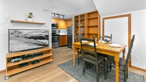 Eine moderne Küche mit integrierten Geräten, ein Essbereich mit Holztisch und -stühlen sowie ein Flachbildfernseher auf einem Holzständer.