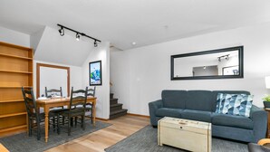 Ein modernes Wohnzimmer mit Essbereich, einer Couch, einem Couchtisch und einer Treppe, die eine weitere Ebene hinaufführt.