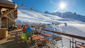 Une terrasse en bois, agrémentée de tables et de chaises, qui offre une vue sur un paysage montagneux enneigé.