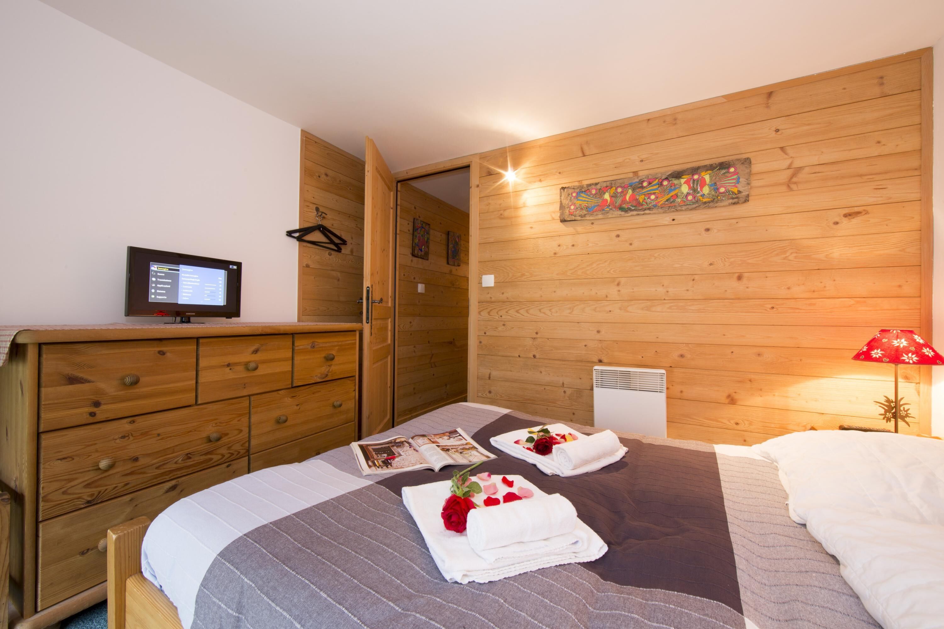 Une chambre à coucher aux murs lambrissés, avec un lit, un téléviseur et une lampe rouge.