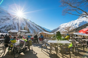A wooden deck with tables and chairs, overlooking a snowy mountain landscape.