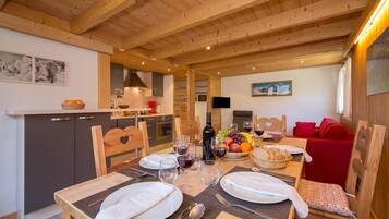 Un intérieur en bois avec une table à manger dressée pour deux personnes, un coin cuisine et un canapé rouge.