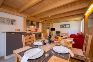 A wooden interior with a dining table set for two, a kitchen area, and a red sofa. - Grand Roc A218 150m from Slopes, View & Parking, Argentière (Chamonix), France (Argentière (Chamonix))