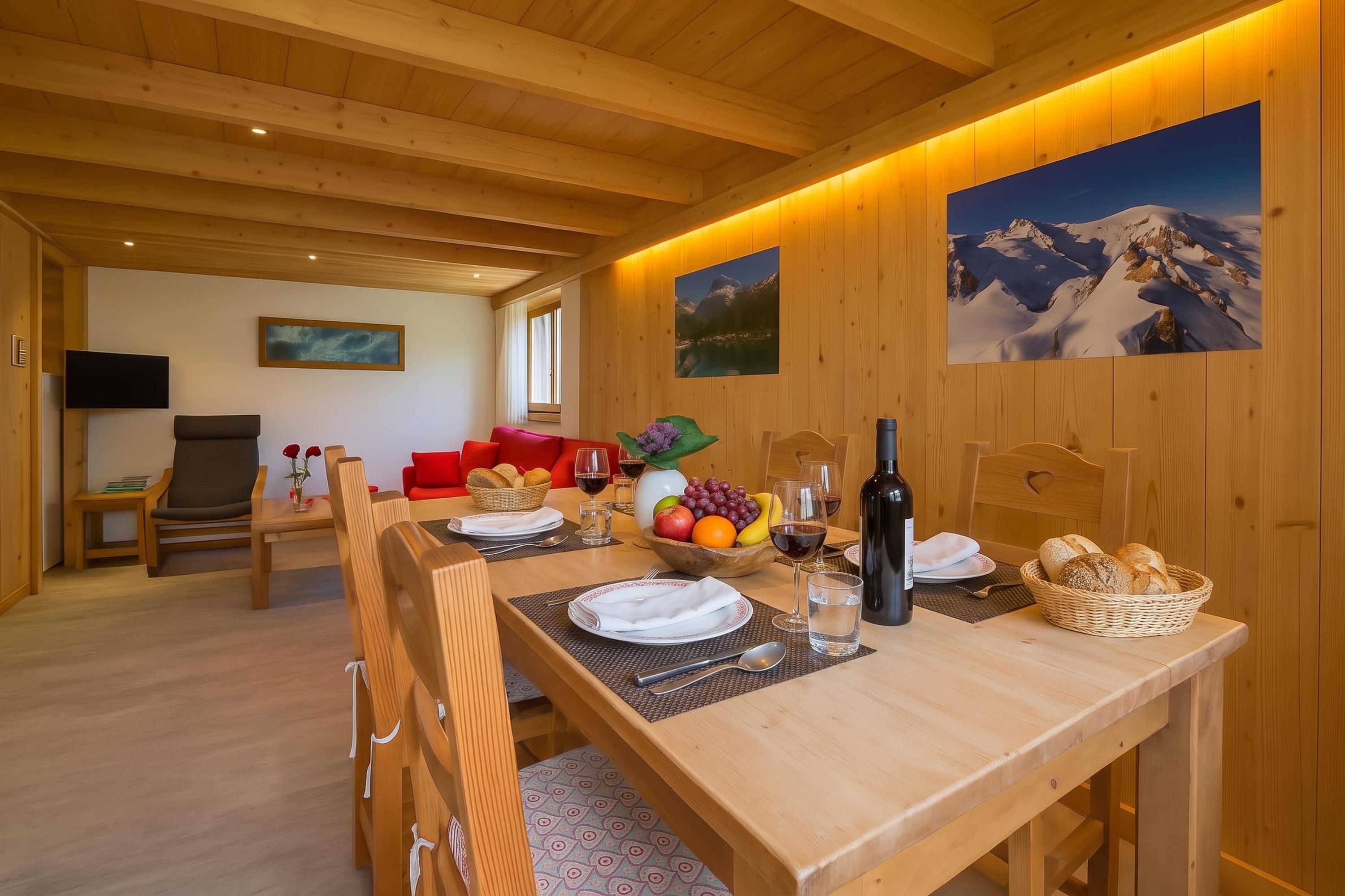 Un coin repas en bois avec une table dressée pour quatre personnes, un canapé et un téléviseur en arrière-plan.