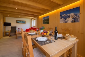 Un comedor de madera con una mesa dispuesta para cuatro, un sofá y un televisor al fondo.