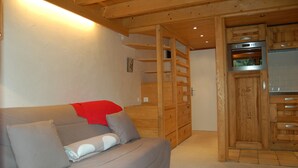 A wooden interior with a sofa, a wooden cabinet, and a kitchen area. - Grand Roc A104 150m from Slopes, Parking & WiFi, Argentière (Chamonix), France (Argentière (Chamonix))