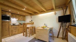 A wooden kitchen with a built-in oven, wooden cabinets, a dining table with chairs, a television mounted on the wall, and a window with curtains. - Grand Roc A104 150m from Slopes, Parking & WiFi, Argentière (Chamonix), France (Argentière (Chamonix))