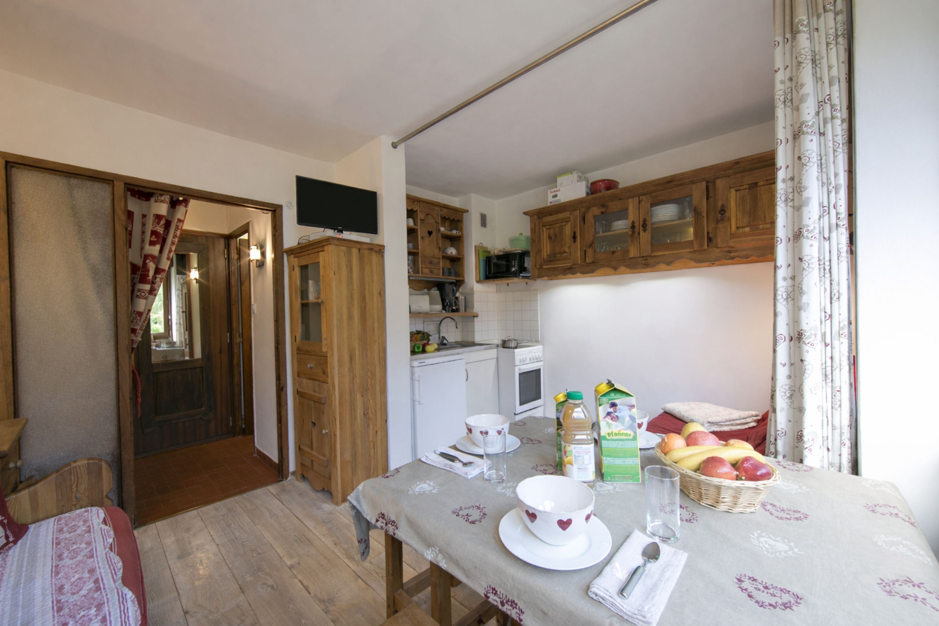 Une cuisine compacte avec des meubles en bois, un four à micro-ondes et une table à manger dressée avec des assiettes, des bols et un panier de fruits.