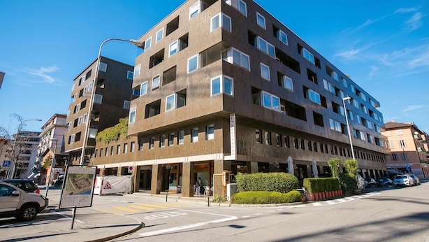 Un immeuble à plusieurs étages, doté d’un style architectural moderne, avec une entrée au niveau du sol, un espace abrité et une enseigne bien visible.
