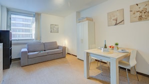 Un salon moderne avec un canapé gris, une table à manger avec des chaises, un meuble blanc et des œuvres d’art accrochées au mur.