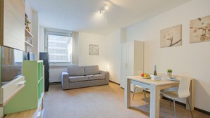 Une pièce moderne et bien éclairée, avec un canapé gris, une table à manger et des chaises, ainsi qu’un petit meuble.