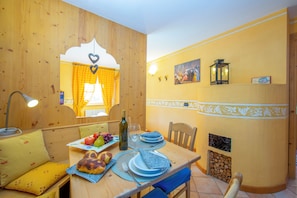 A wooden interior with a dining table set, a window with curtains, and a wall-mounted picture.