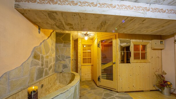 A stone bathtub with a candle, wooden walls, and a wooden door leading to another room. - Perla Ski in, Livigno, Italy (Livigno)