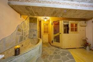 A stone bathtub with a candle, wooden walls, and a wooden door leading to another room. - Perla Ski in, Livigno, Italy (Livigno)
