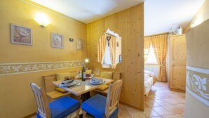A dining area with a wooden table, blue cushioned chairs, and a bench. There are framed pictures on the wall, a light fixture above the table, and a window with curtains. - Perla Ski in, Livigno, Italy (Livigno)