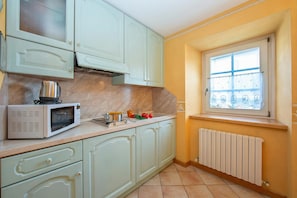 A kitchen with a microwave, sink, and window with blinds.