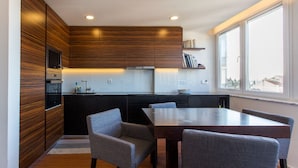 A modern kitchen with dark wood cabinets, a built-in oven, and a dining area with a table and chairs. - Cozyplace 23 in Lisbon - 1 bedroom appartment (Lisboa)