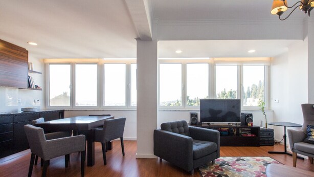 A modern living room with a dining area, large windows, a flat-screen TV, and a kitchen area. - Cozyplace 23 in Lisbon - 1 bedroom appartment (Lisboa)