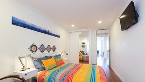 A bedroom with a colorful striped bedspread, a mounted TV, and decorative wall art. - Cozyplace 23 in Lisbon - 1 bedroom appartment (Lisboa)