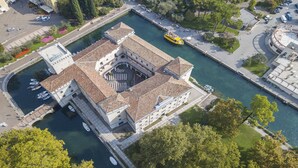 An aerial view of a historic building with a central courtyard, adjacent to a canal, surrounded by greenery and a parking area. - Appartamento Villa Lina with Lake View, Riva del Garda, Italy (Riva del Garda)