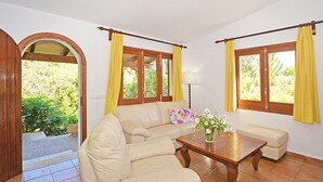 Een woonkamer met een beige bank, een houten salontafel, gele gordijnen en uitzicht op groen.