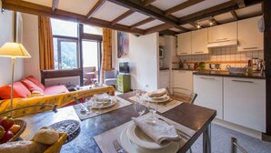 A dining area with a table set for four, a sofa, and a kitchen in the background. - Grand Roc B207 260m from Slopes, View, Parking & WiFi, Argentière (Chamonix), France (Argentière (Chamonix))