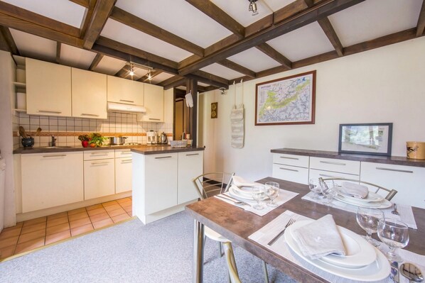 Une cuisine avec des meubles blancs, un plafond en bois et un coin repas avec une table mise pour quatre personnes.