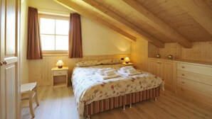 A wooden-paneled bedroom with a bed, bedside tables, a chair, and a window with curtains. - Arcobaleno, Livigno, Italy (Livigno)