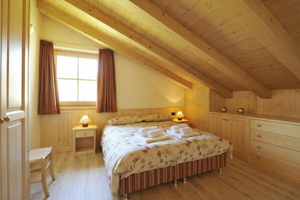 Une chambre à coucher aux murs lambrés, avec un lit, des tables de chevet, une chaise et une fenêtre avec des rideaux.