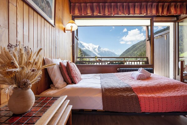 Une pièce en bois avec un lit, un vase contenant des plantes séchées et une vue sur les montagnes.