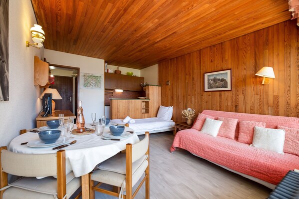 Una habitación acogedora con techo de madera, una mesa de comedor con sillas, un sofá rosa y una cama.