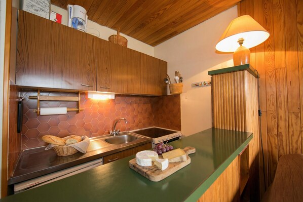 Uma cozinha com armários de madeira, bancada verde, pia, fogão e uma luminária.