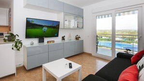 A modern living room with a television, a sofa, a coffee table, and a view of a swimming pool through a glass door. - LOS JUNCOS HomeStay by Turismar (La Pineda)