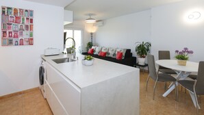 A modern kitchen with a built-in island, a dining area with a round table and chairs, and a living area with a sofa and decorative pillows. - LOS JUNCOS HomeStay by Turismar (La Pineda)