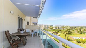 A balcony with a table and chairs, a potted plant, and a view of a green landscape with buildings in the distance. - LOS JUNCOS HomeStay by Turismar (La Pineda)