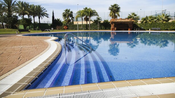 A swimming pool with a tiled deck, palm trees, and a clear sky. - LOS JUNCOS HomeStay by Turismar (La Pineda)