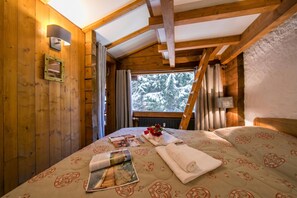 Une pièce chaleureuse en bois, avec un lit, une fenêtre avec des rideaux et une lampe fixée au mur.
