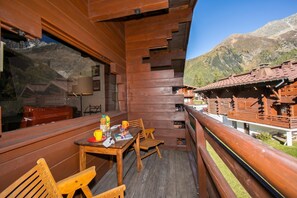 Ein Holzbalkon mit Tisch und Stühlen mit Blick auf eine gebirgige Landschaft.