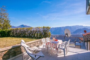 A terrace with a table and chairs, a stone wall, and a view of mountains.