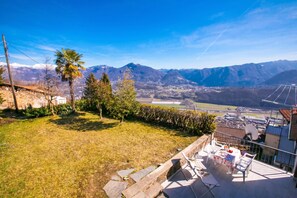 A balcony with a table and chairs, overlooking a mountainous landscape with a clear sky.